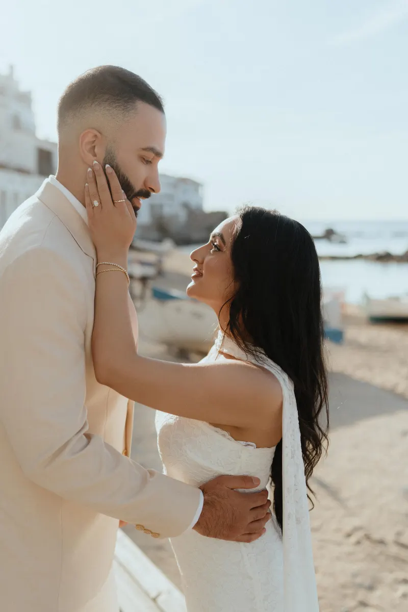 Couple embraces on a sunlit beach after a surprise proposal, capturing joy and romance in a candid photoshoot moment.