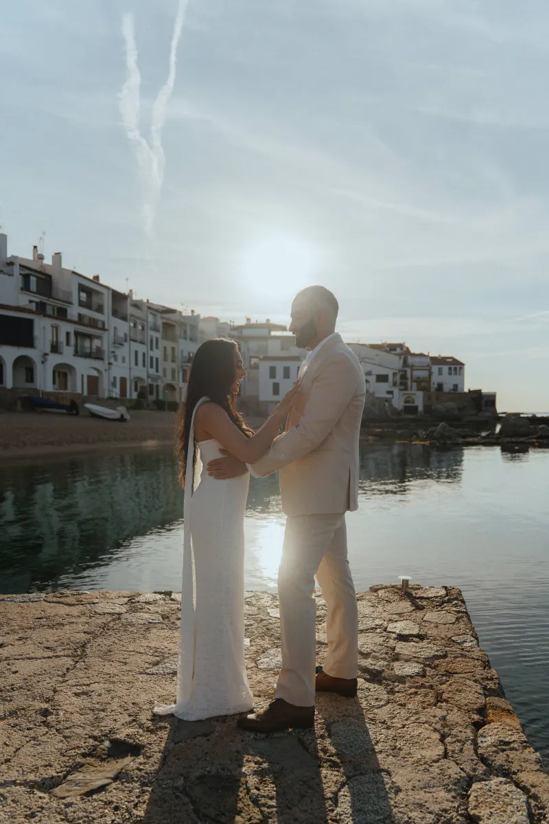Couple embraces on a sunlit pier during a surprise proposal photoshoot by the waterfront in a charming coastal village.