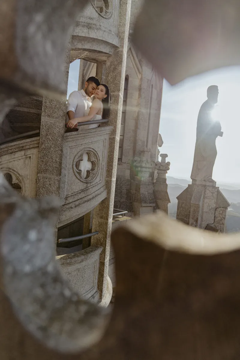 Couple embraces on a sunlit stone balcony of a historic building during a romantic couples & engagements photoshoot.
