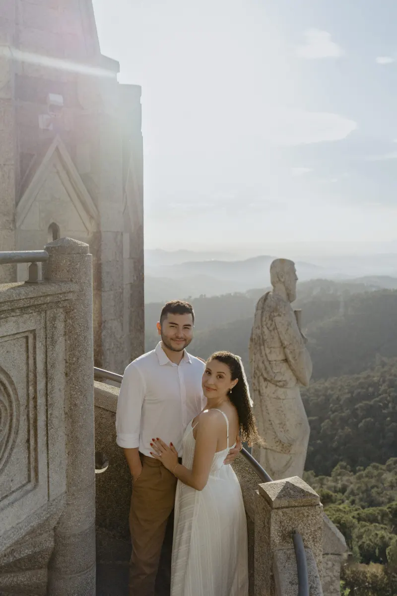 Couple embraces on a sunlit stone balcony overlooking mountains, captured during a romantic couples & engagements photoshoot.