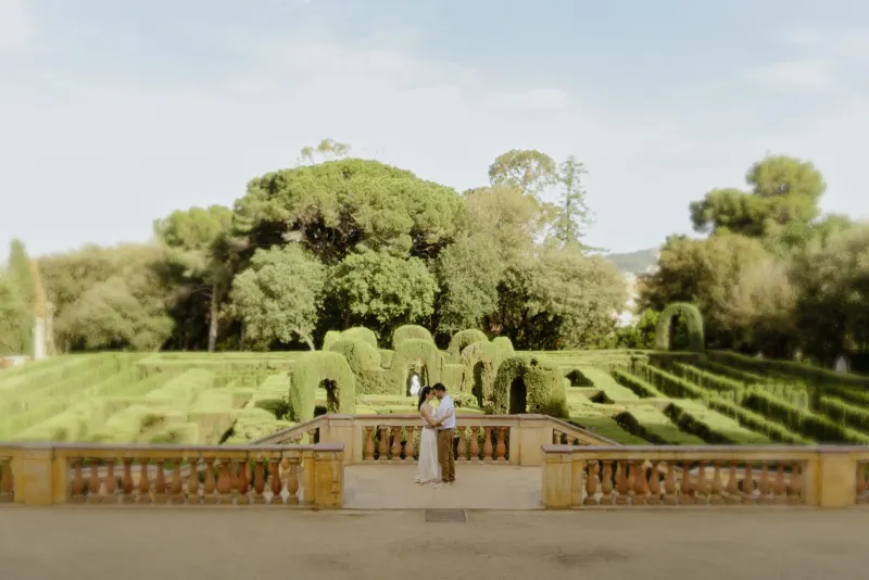 Couple embraces on a sunlit terrace overlooking a lush garden maze during a couples & engagements photoshoot.