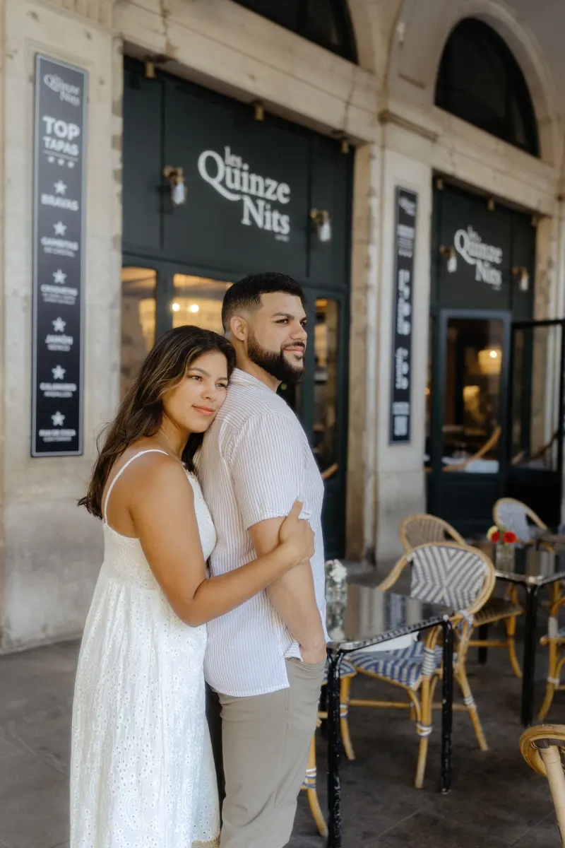 Couple embraces outside a charming café, sharing a quiet moment during their couples & engagements photoshoot.