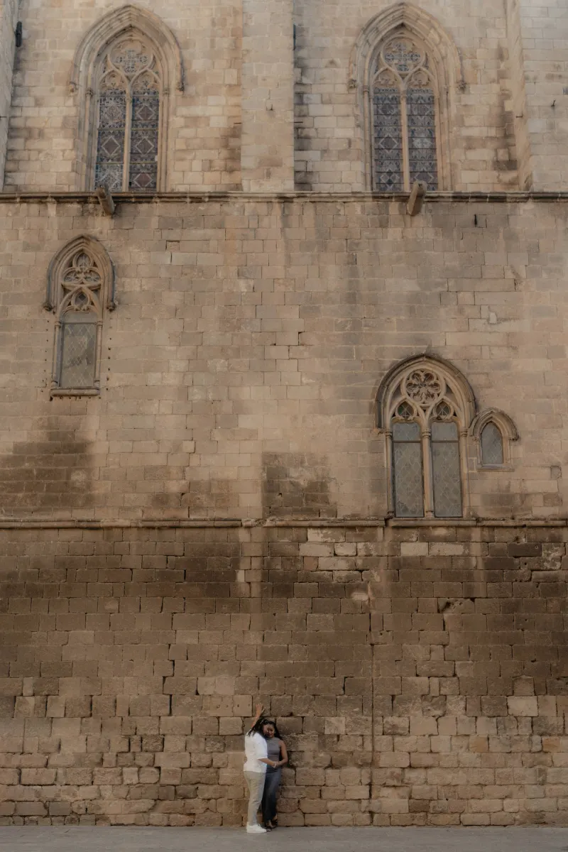 Couple embraces tenderly against a historic stone wall in Barcelona during their surprise proposal photoshoot.