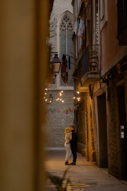 Couple embraces under string lights in a quiet Barcelona alley during a couples & engagements photoshoot.