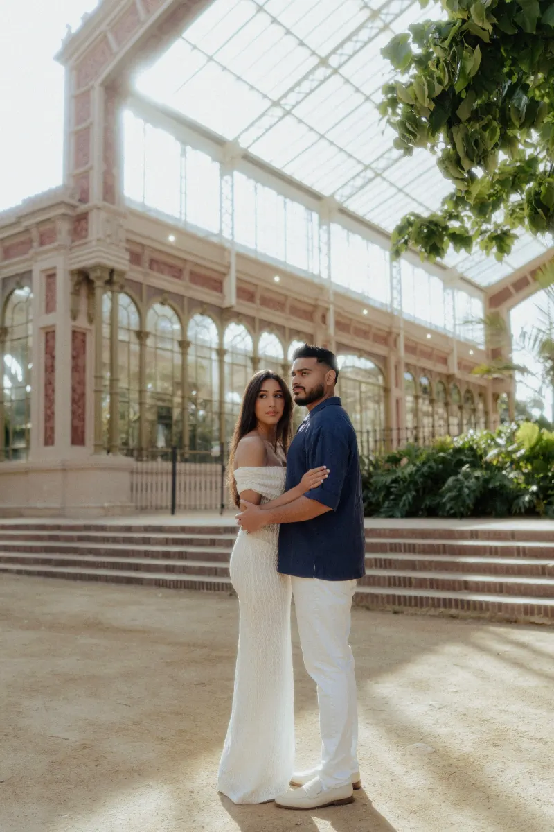 Couple embracing and gazing softly in front of a grand glass conservatory during a couples & engagements photoshoot.