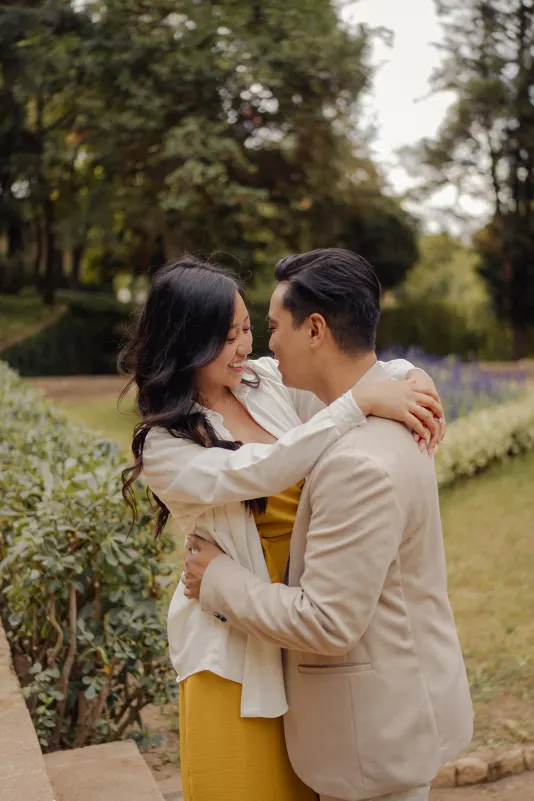 Couple embracing and laughing together in a lush garden during an outdoor engagement photoshoot session.