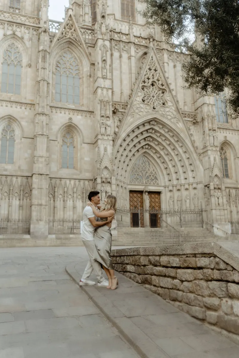 Couple embracing and smiling in front of Barcelona’s cathedral during a Vacation Portraits photoshoot.