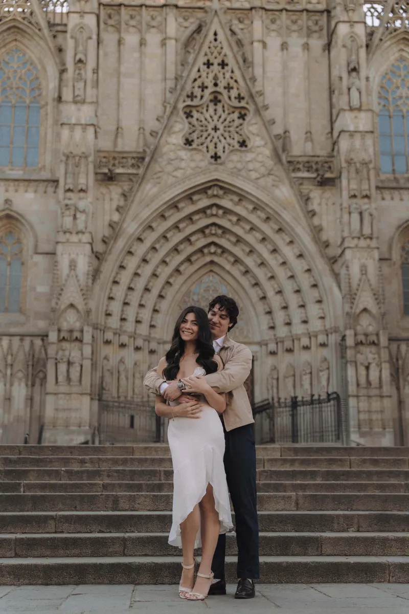 Couple embracing and smiling on cathedral steps, celebrating their engagement during a couples photoshoot.