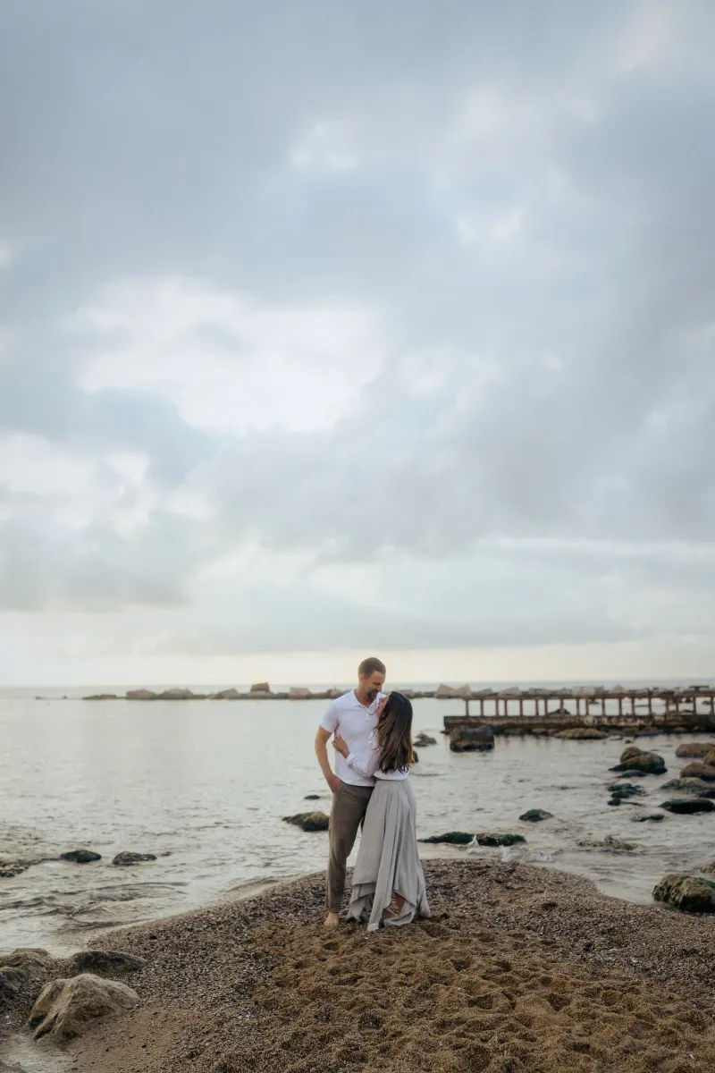 Couple embracing on a quiet beach at dusk, sharing a tender moment during an engagement photoshoot session.