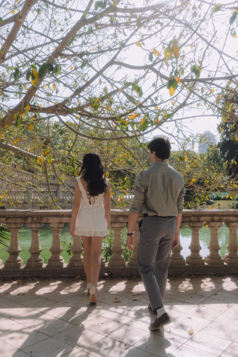 Couple enjoying a peaceful stroll by the water under sun-dappled trees during a couples & engagements photoshoot.