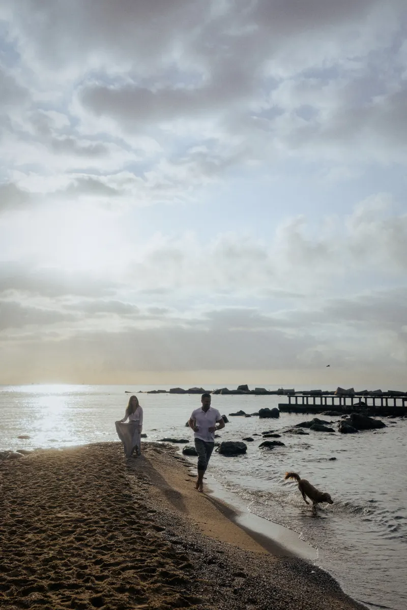 Couple enjoying a relaxed stroll along the shoreline with their dog during a couples & engagements photoshoot at the beach.