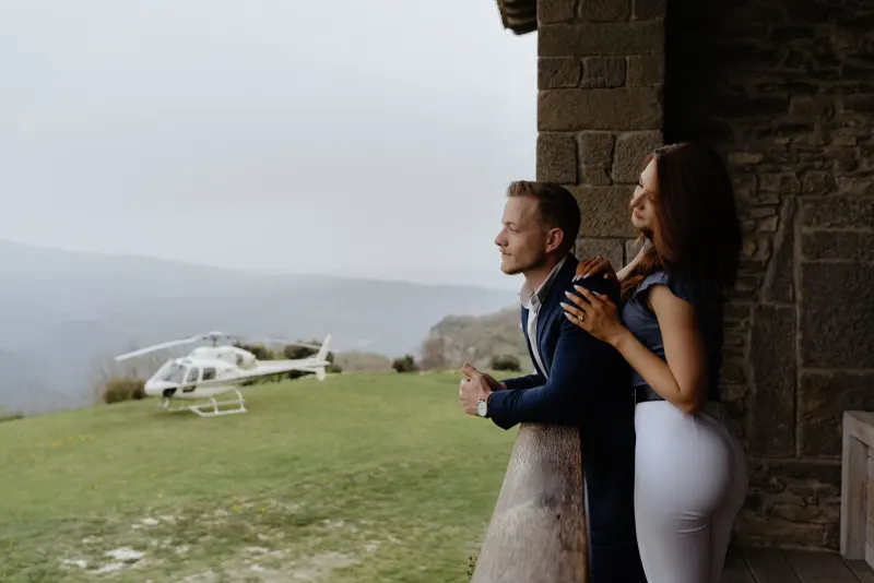 Couple enjoys a quiet, romantic moment on a rustic balcony after arriving by helicopter for their surprise proposal photoshoo