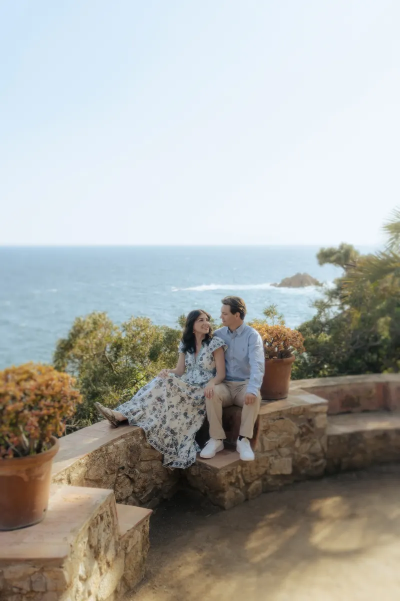 Couple gazes at each other on a stone terrace by the sea, captured during a surprise proposal photoshoot.