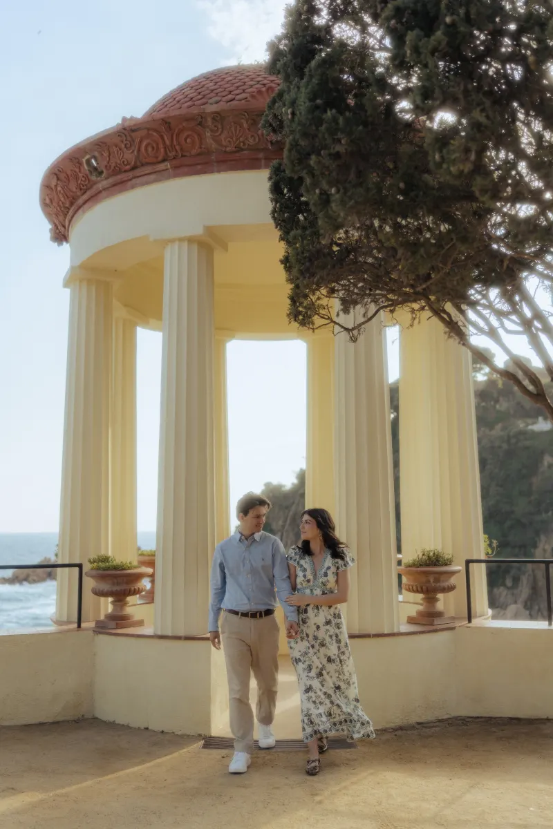 Couple gazes at each other while walking near a Mediterranean pavilion during their surprise proposal photoshoot.