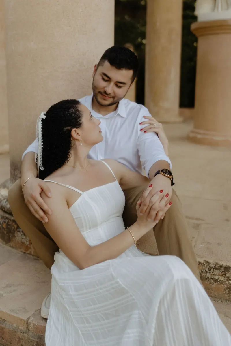 Couple gazes lovingly at each other while seated on stone steps, captured during a couples & engagements session at a pavilio