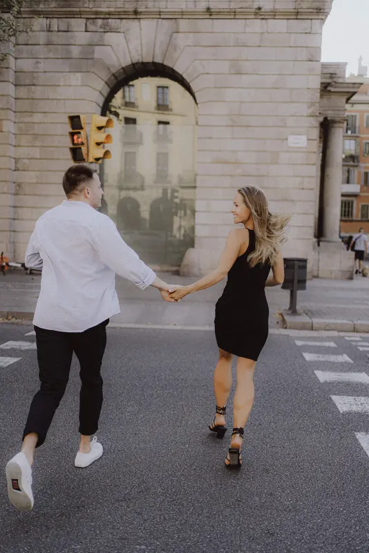 Couple holding hands and laughing as they cross a city street, captured during a couples & engagements photoshoot.