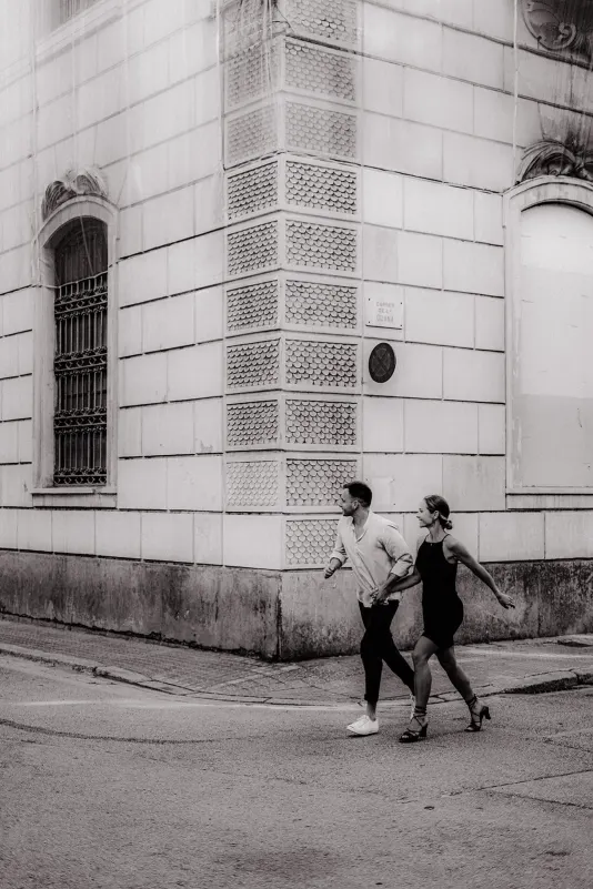 Couple holding hands and laughing as they cross a quiet city street during a couples & engagements photoshoot.