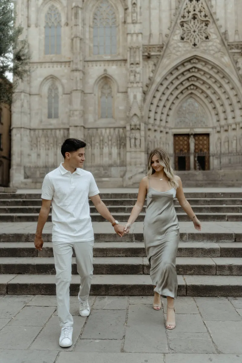 Couple holding hands and laughing as they descend cathedral steps in Barcelona, captured during a Vacation Portraits session.
