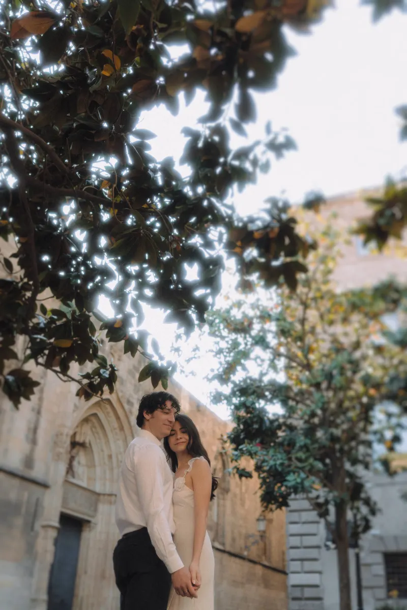 Couple holding hands and sharing a peaceful embrace beneath leafy trees during a couples & engagements photoshoot.