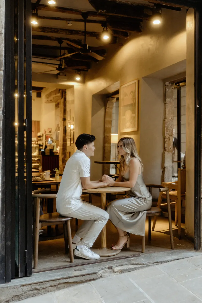 Couple holding hands and sharing a warm conversation at a cozy Barcelona café during a Vacation Portraits session.