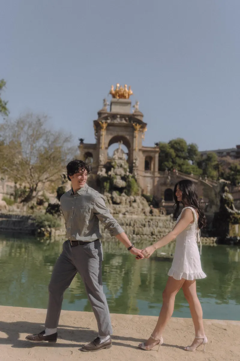 Couple holding hands and smiling as they walk by the fountain at Parc de la Ciutadella during an engagement photoshoot.
