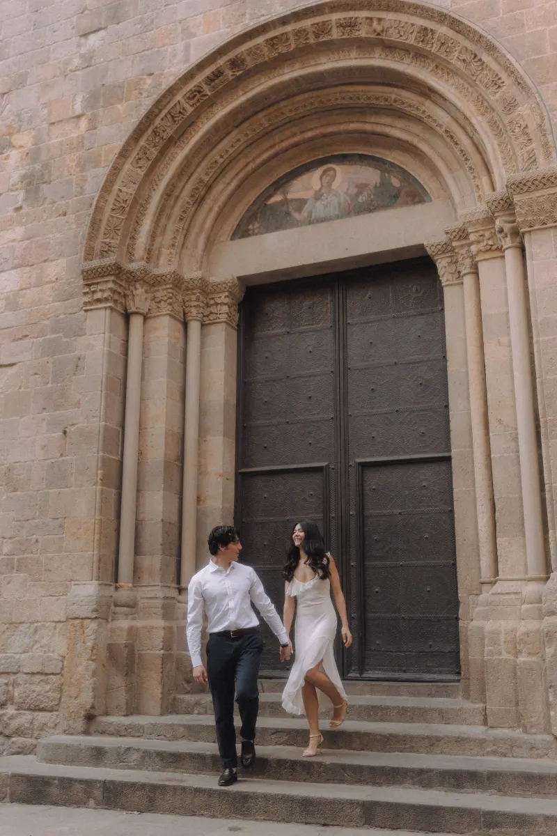 Couple holding hands and smiling as they walk down historic stone steps during a couples & engagements photoshoot.