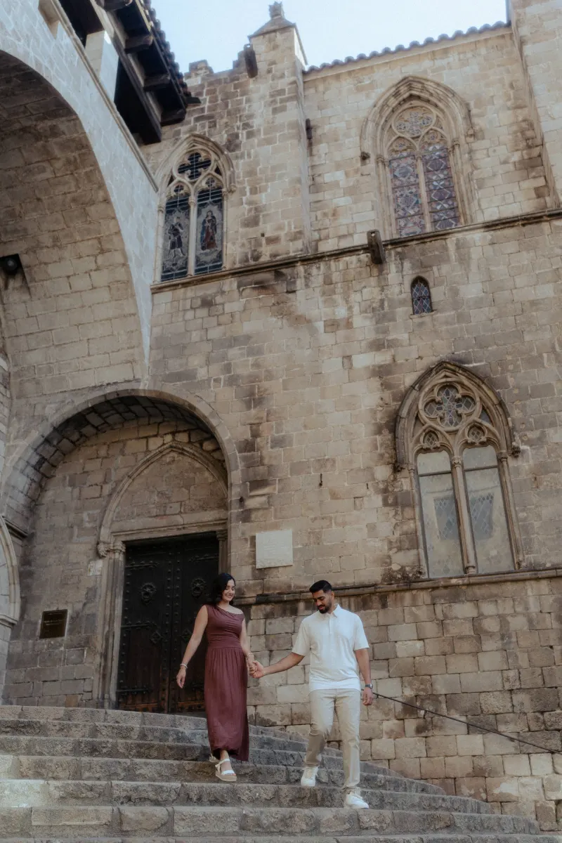 Couple holding hands and smiling as they walk down stone steps during a couples & engagements photoshoot in a historic square