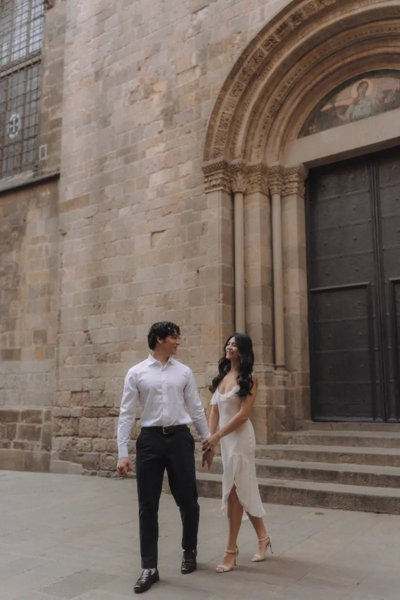 Couple holding hands and smiling as they walk past a historic stone doorway during a couples & engagements photoshoot.