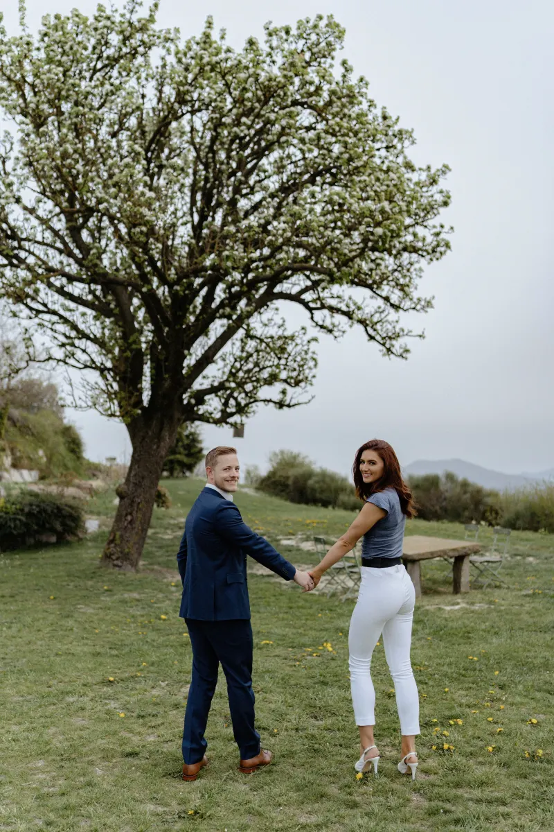Couple holding hands and smiling as they walk through a scenic countryside, captured during a surprise proposal photoshoot.