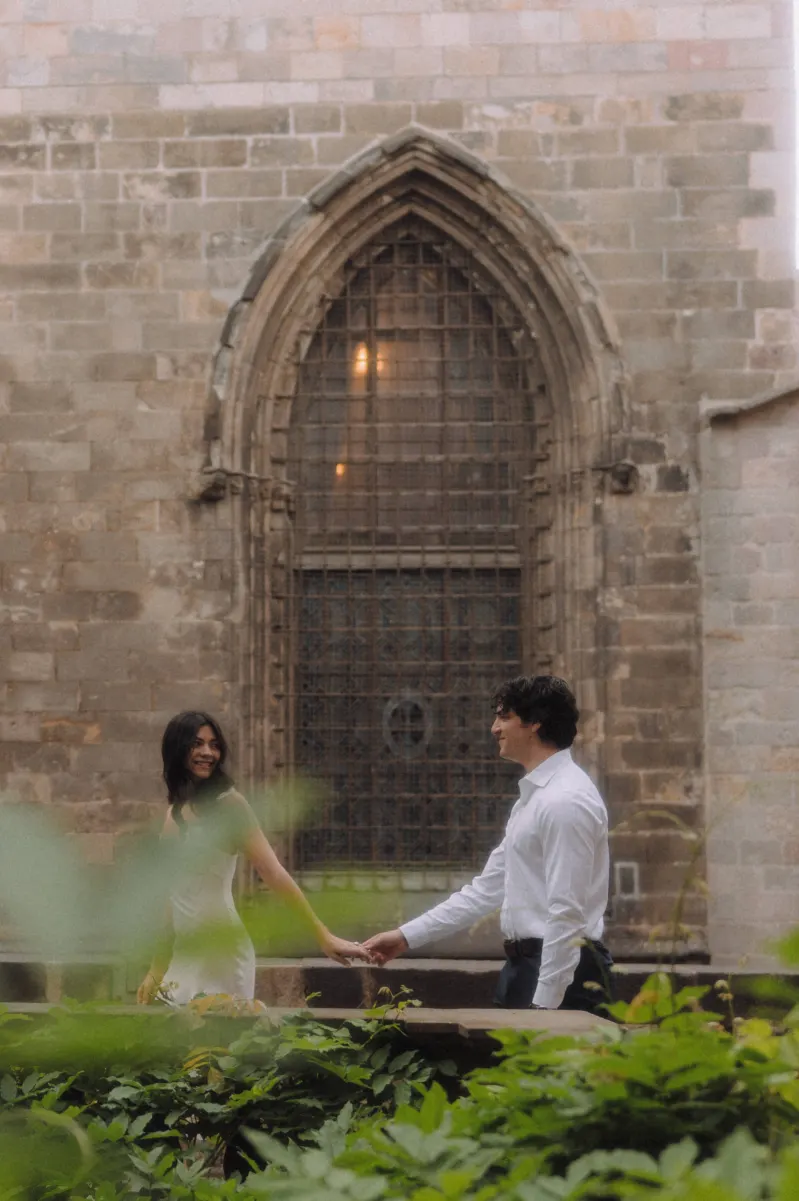 Couple holding hands and smiling at each other in a historic courtyard during a couples & engagements photoshoot.