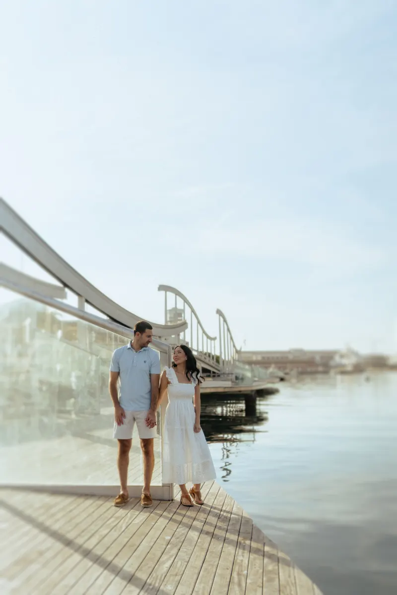 Couple holding hands and smiling at each other on a sunny marina boardwalk during a couples & engagements photoshoot.