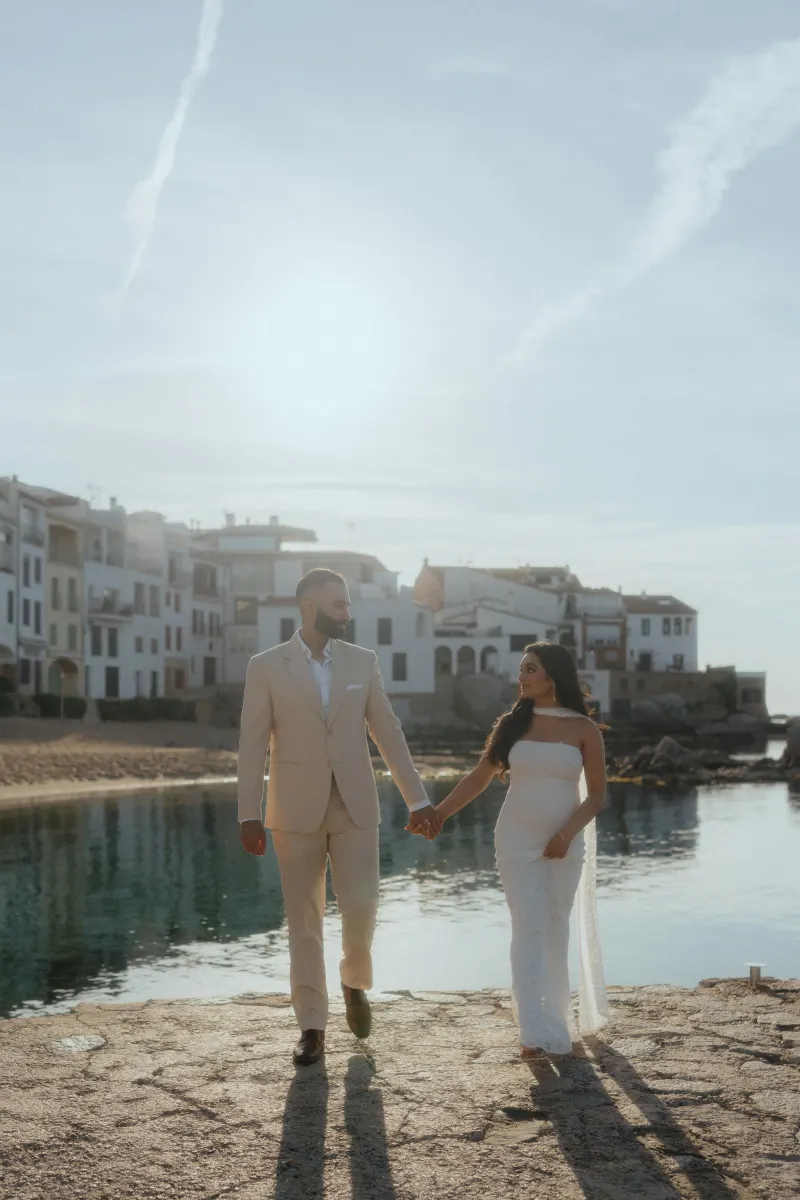 Couple holding hands and smiling during a surprise proposal photoshoot by the water in a charming coastal village.