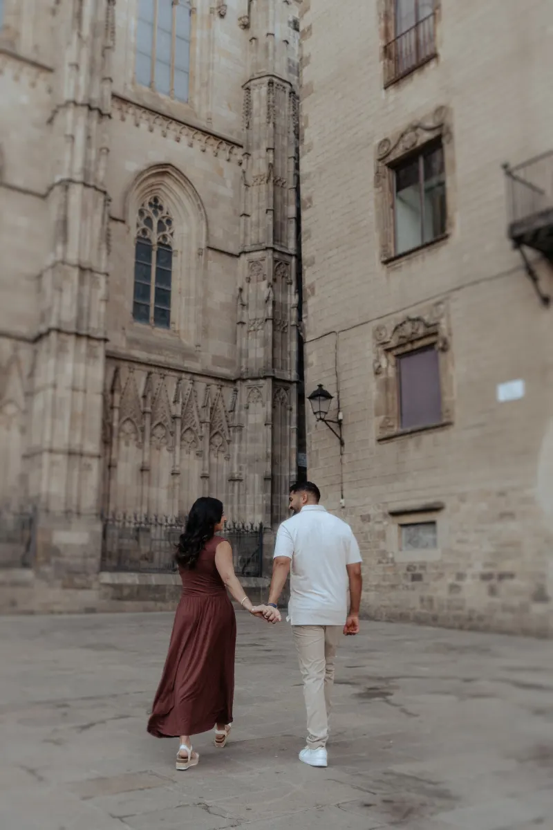 Couple holding hands and smiling during an engagement photoshoot in a historic European city street.