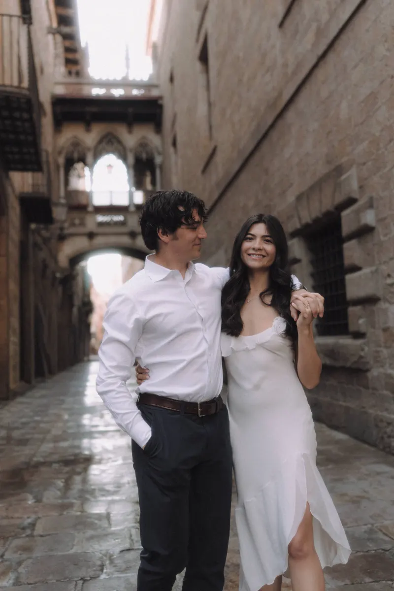 Couple holding hands and smiling in a romantic Gothic Quarter alley during a couples & engagements photoshoot.