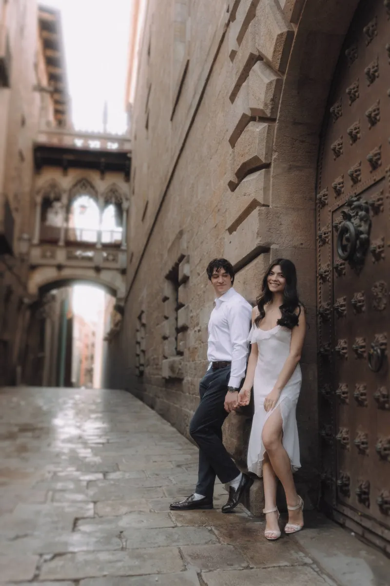 Couple holding hands and smiling in a romantic Gothic Quarter alley during a couples & engagements photoshoot in Barcelona.
