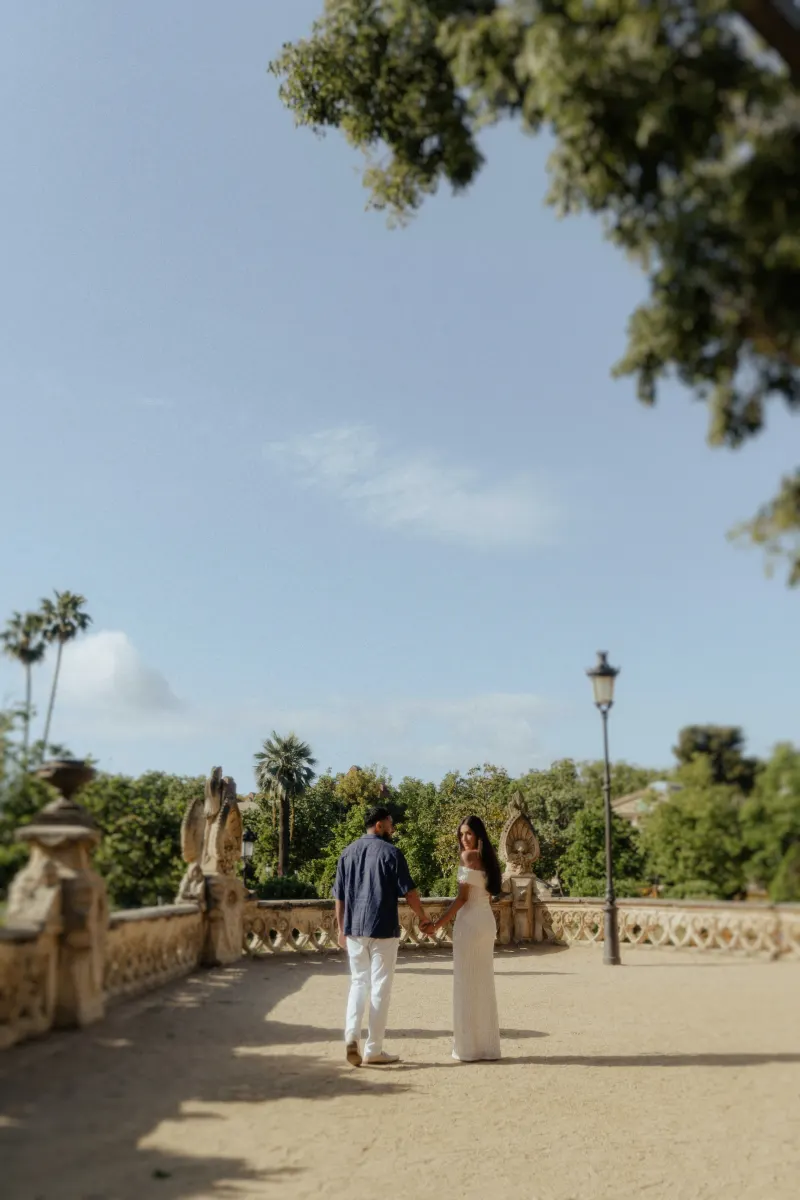 Couple holding hands and smiling in a sunlit garden courtyard during a romantic couples & engagements photoshoot.