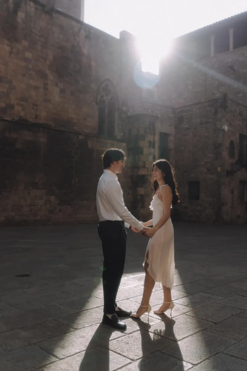 Couple holding hands and smiling in soft sunlight, sharing a romantic moment during a couples & engagements photoshoot.