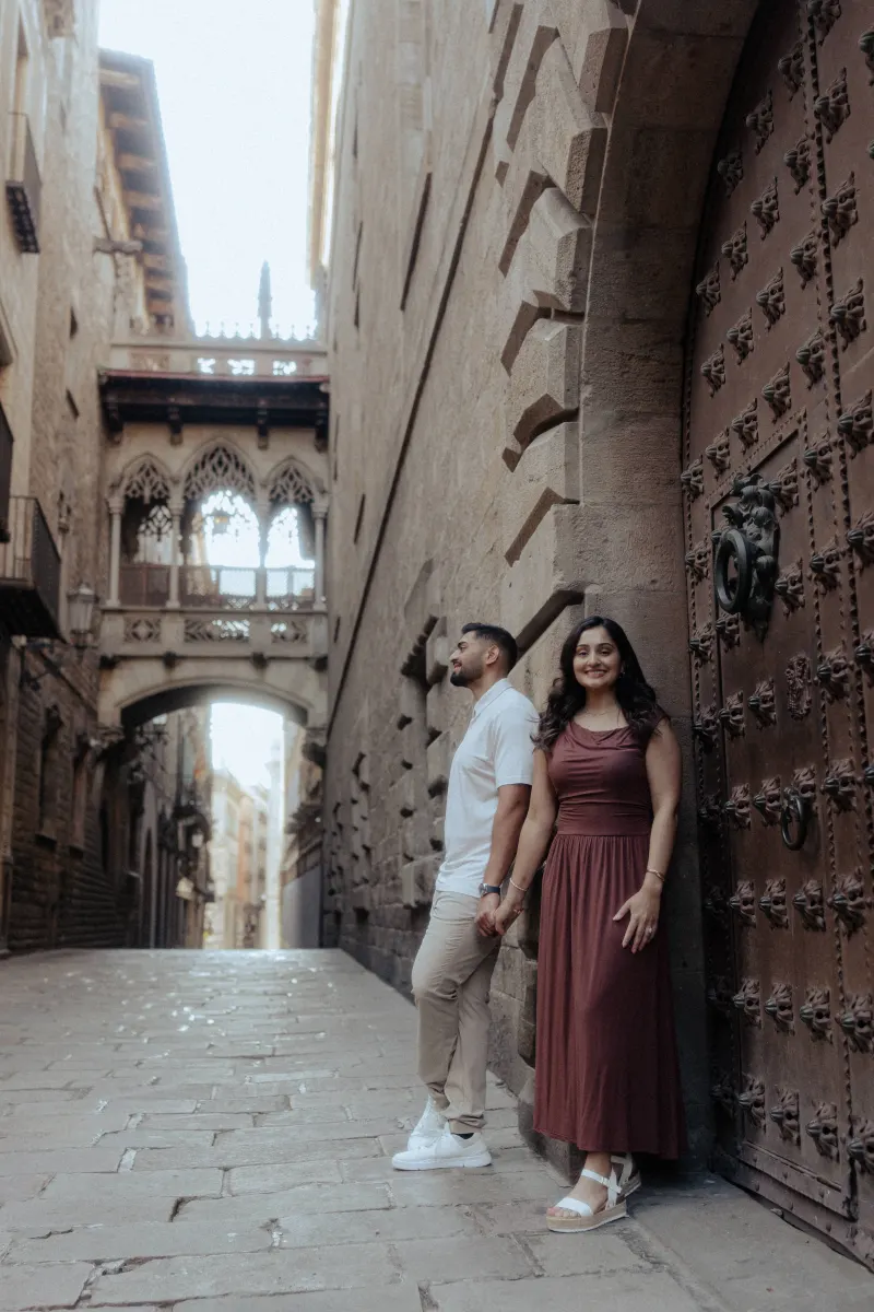 Couple holding hands and smiling softly during a couples & engagements photoshoot in a historic European alleyway.