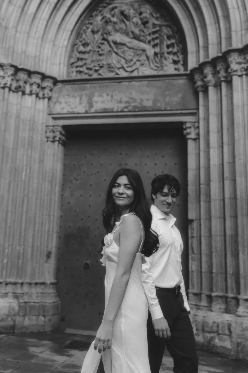 Couple holding hands and smiling softly in front of a grand cathedral door during a couples & engagements photoshoot.