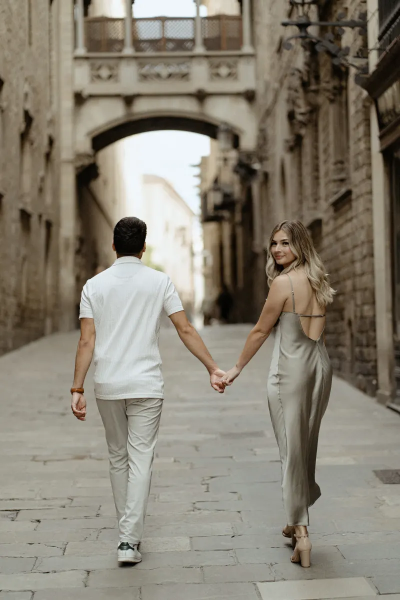 Couple holding hands and strolling through Barcelona’s Gothic Quarter, she smiles back during a Vacation Portraits session.