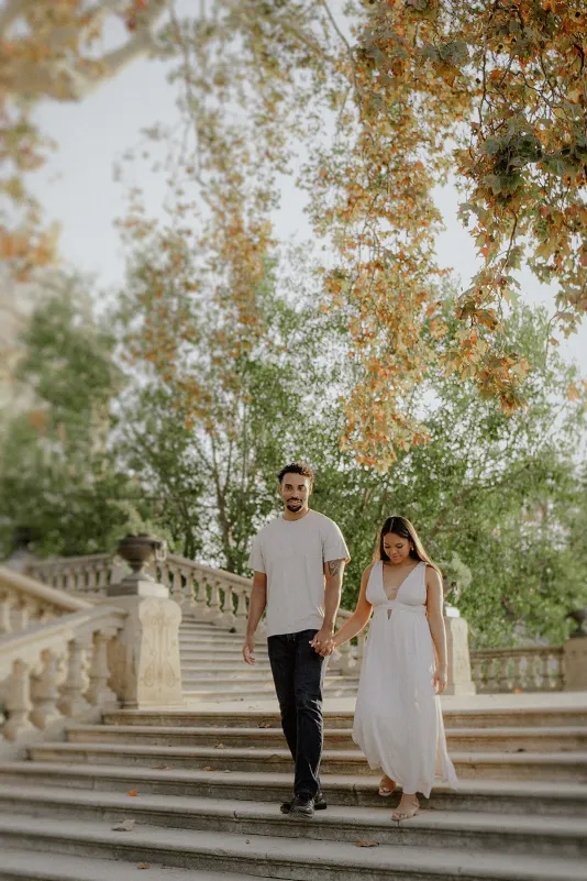 Couple holding hands and walking down stone steps, sharing a peaceful moment during an engagement photoshoot in the park.
