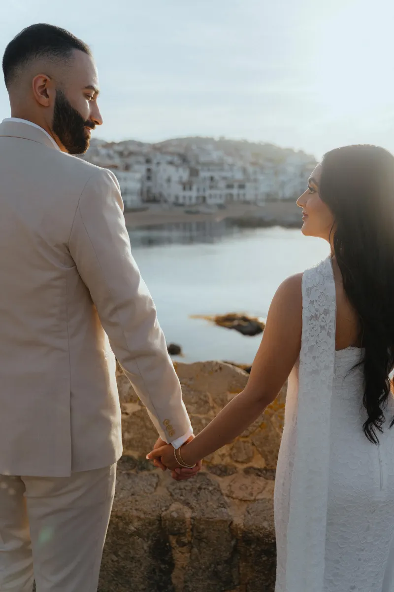 Couple holding hands at sunset by the water, sharing a joyful moment during a surprise proposal photoshoot.