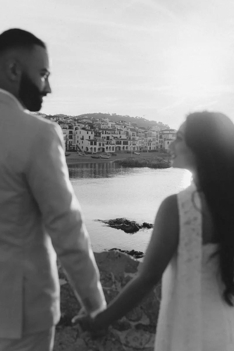 Couple holding hands by the water at sunset during a surprise proposal photoshoot in a charming coastal village.