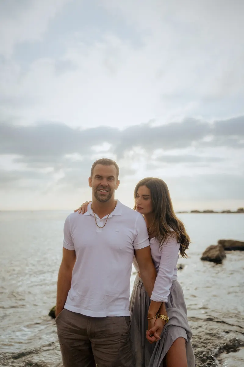 Couple holding hands by the water’s edge at sunset, sharing a quiet moment during a couples & engagements photoshoot.