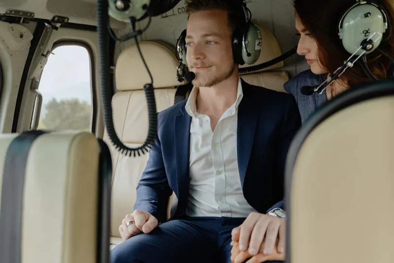 Couple holding hands in a helicopter, capturing anticipation before a surprise proposal photoshoot in the countryside.
