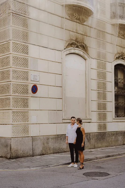 Couple holding hands on a quiet city street, sharing a warm look during a couples & engagements photoshoot.