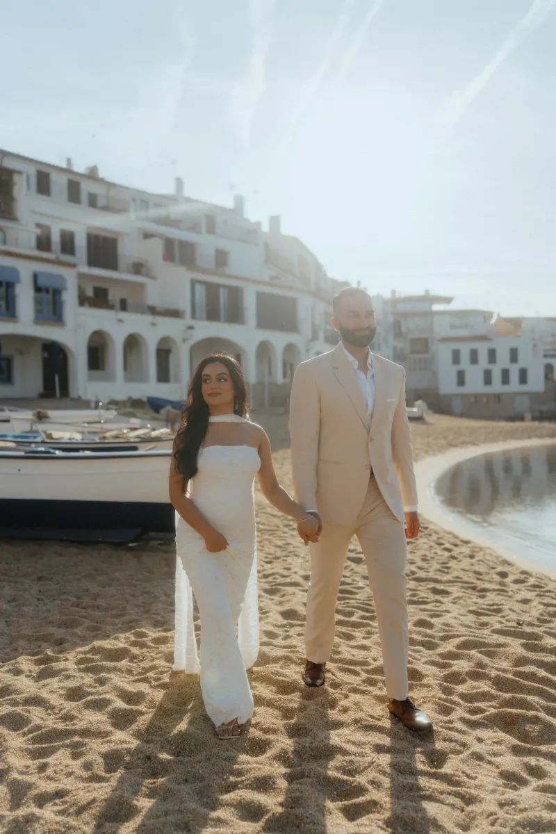Couple holding hands on a sunlit beach, smiling after a surprise proposal photoshoot in a charming coastal village.
