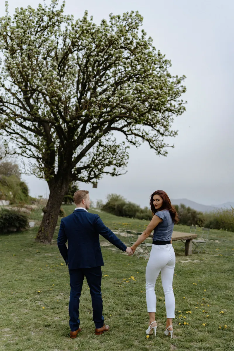 Couple holding hands under a blooming tree, sharing a quiet moment before their countryside surprise proposal photoshoot.