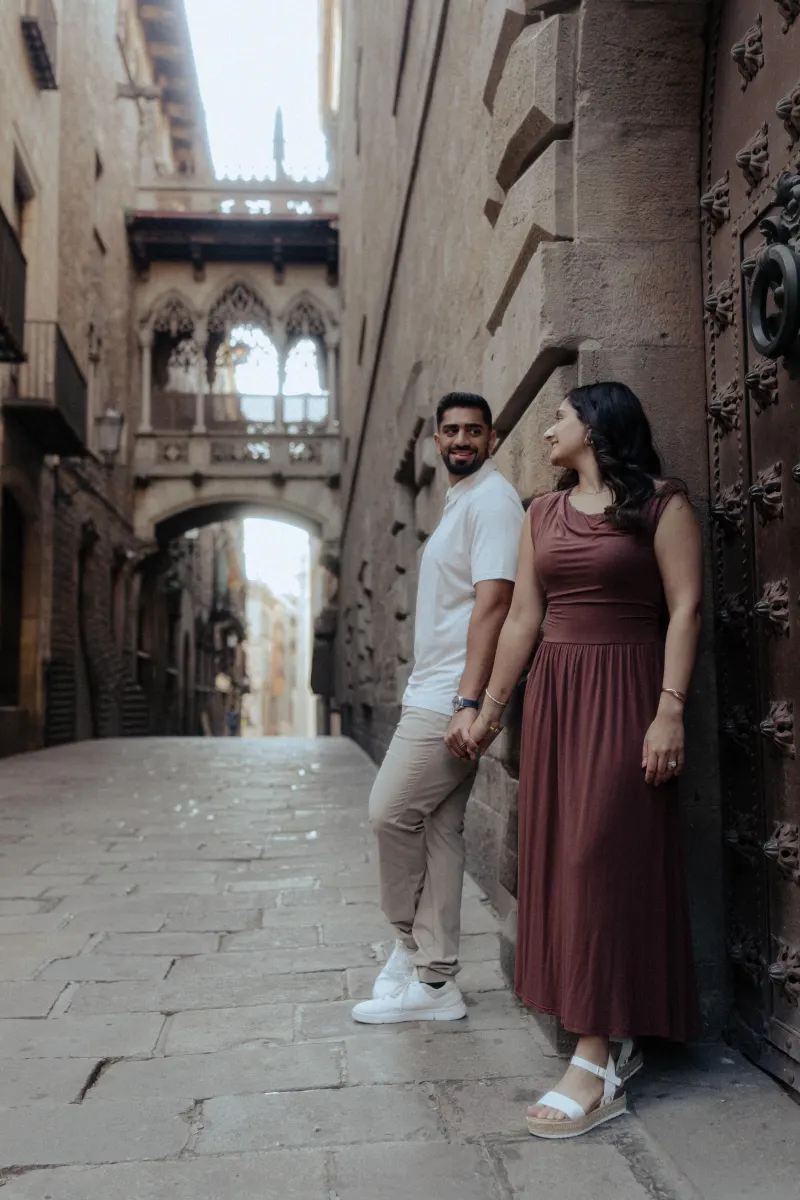 Couple holds hands and smiles at each other during a couples & engagements photoshoot in a historic European alleyway.