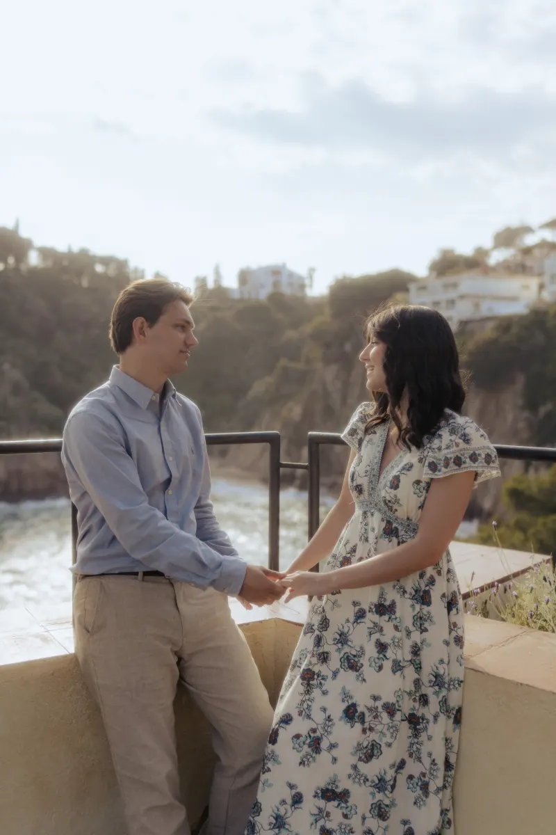 Couple holds hands and smiles at each other on a Mediterranean terrace during a surprise proposal photography session.
